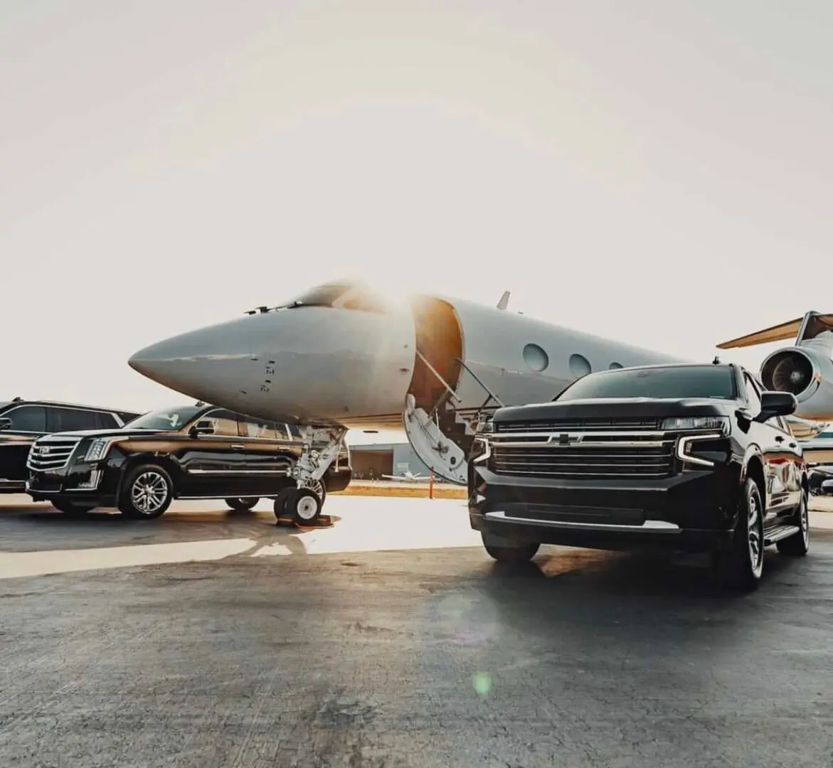 A truck and some cars parked in front of an airplane.