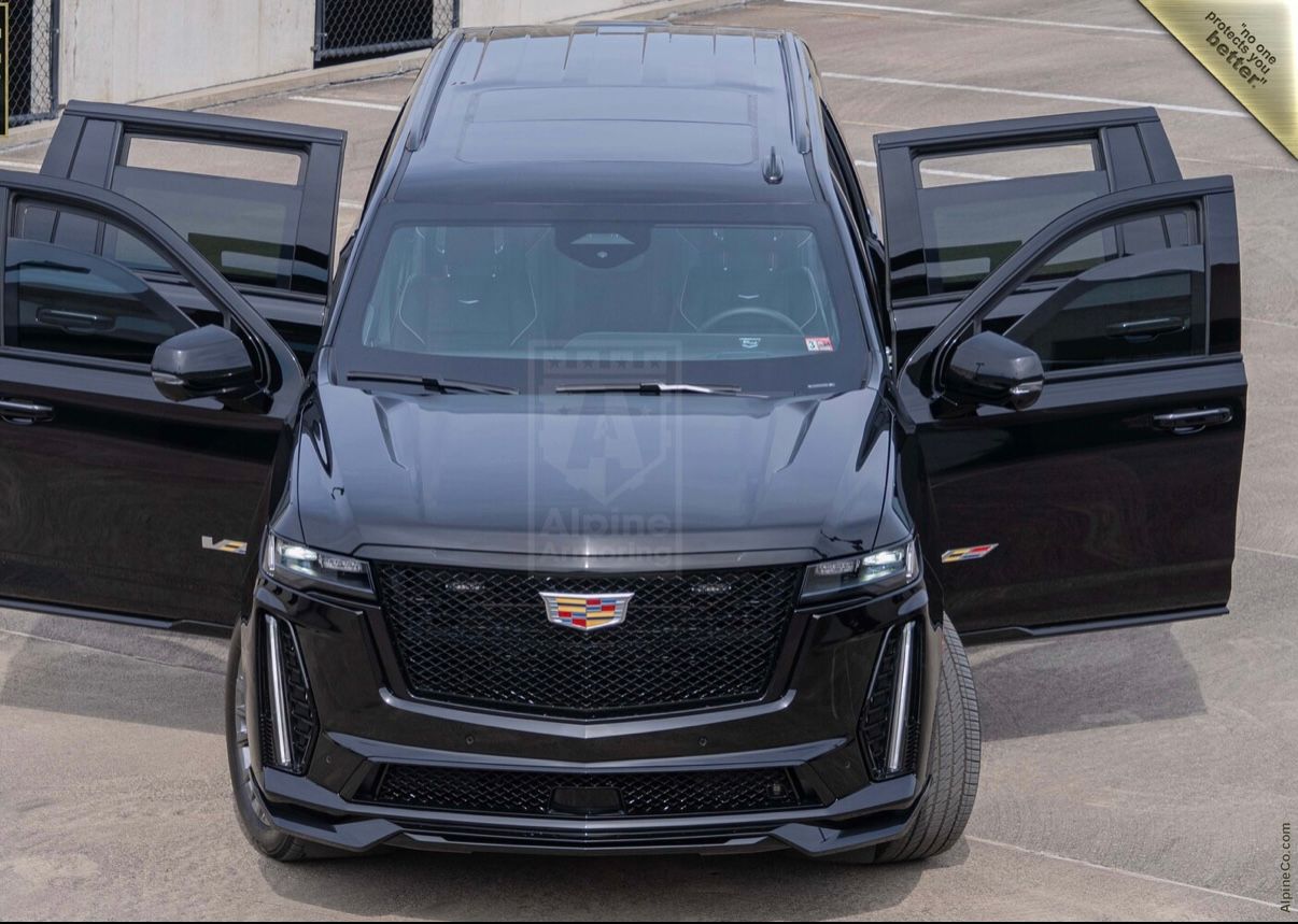 A black cadillac escalade is parked in front of two other cars.